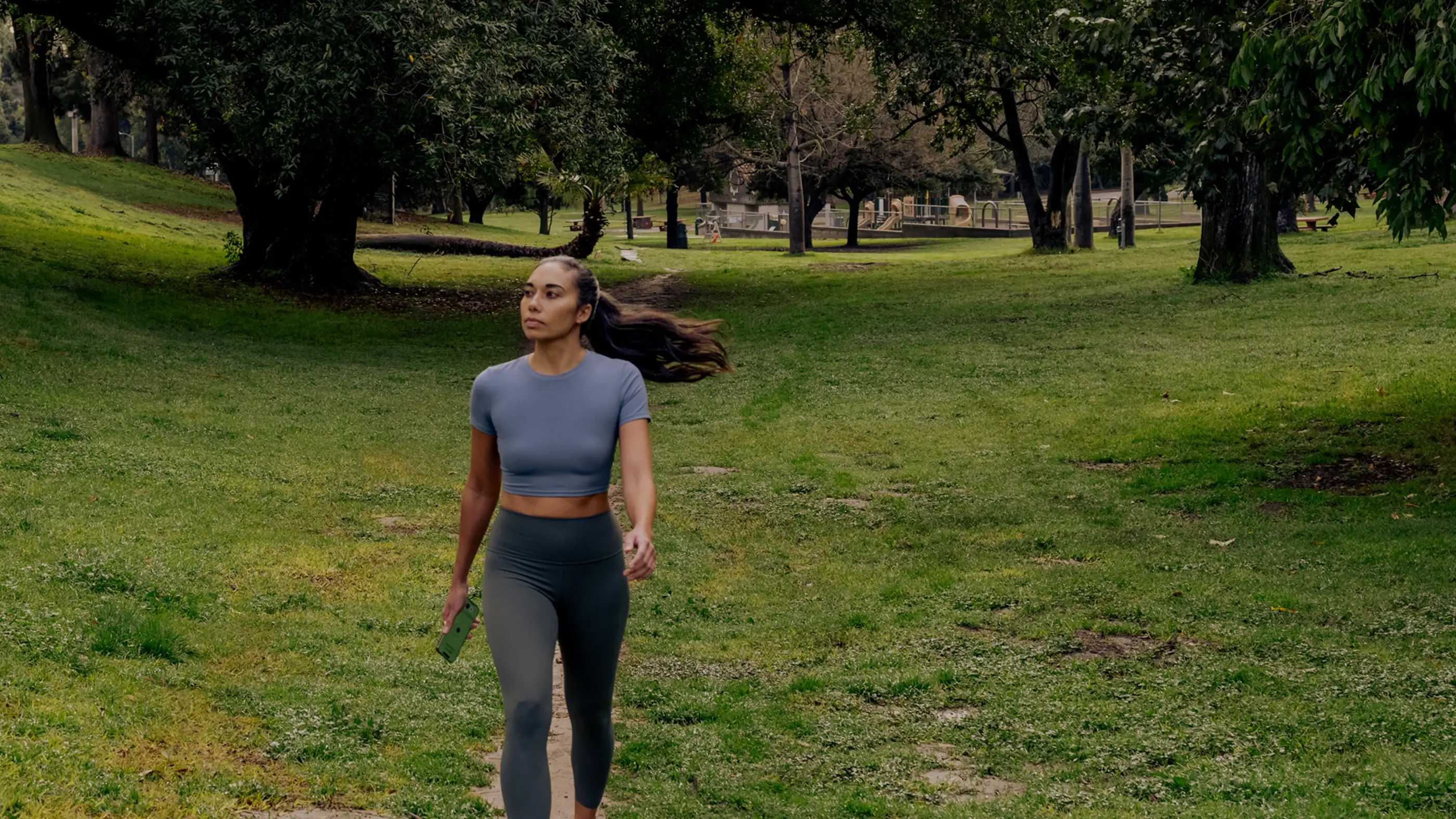 Woman in exercise clothing walks in a park with green grass and trees in the background