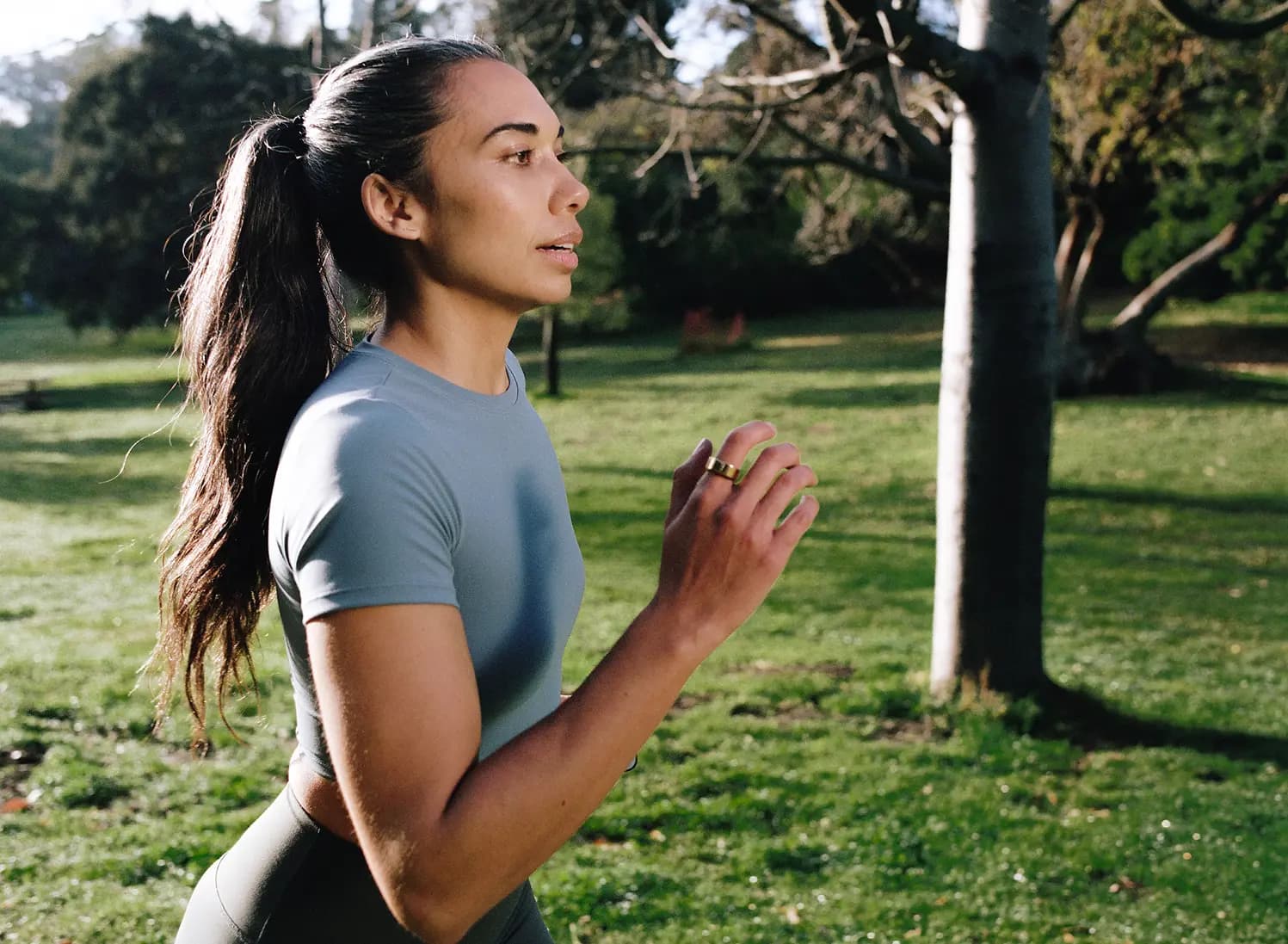 Woman with dark hair on a jog in a grassy park wearing an AlterMe ring on her right hand