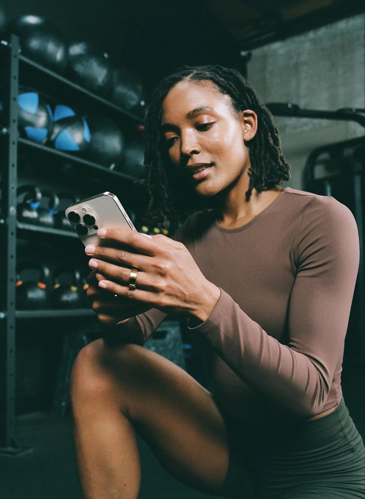 Woman looking at her phone crouching in a room with gym equipment visible in the background